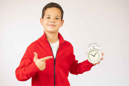 childhood, fashion and people concept - portrait of happy smiling boy in red sweater with alarm clock over white backgroundの写真素材