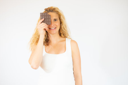 Portrait of a beautiful woman holding chocolate bar at her face isolated over white backgroundの写真素材