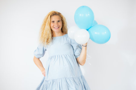 joyful and pregnant woman in blue dress holding balloons isolated on whiteの写真素材