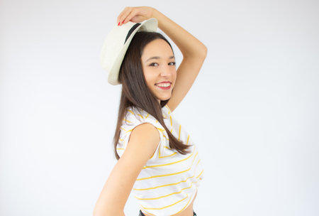girl in striped t-shirt posing with smile on white background. Indoor photo of enthusiastic caucasian woman touching her straw hat.の写真素材