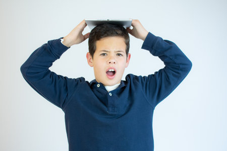 Cute child in a blue shirt holding tablet above his head smiling isolated on white backgroundの写真素材