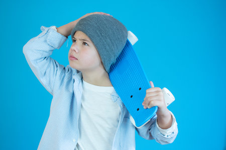 Portrait of pensive guy in casual clothing holding a skateboard on a blue background,の写真素材