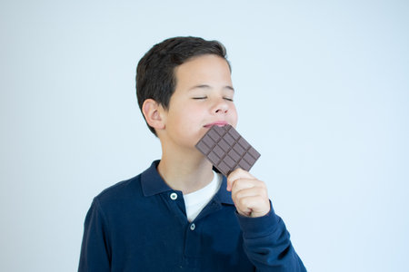 Little kid bites a brown chocolate bar over white background.の写真素材