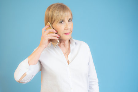 Smiling attractive senior women using a mobile phone over blue background.の写真素材