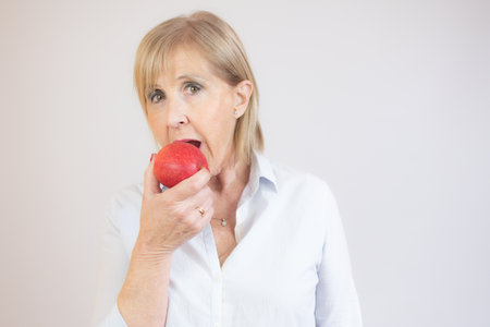 Portrait of senior woman holding an apple by her mouth over white background.の写真素材