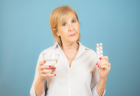 senior woman with glass of water and pills over blue backgroundの写真素材
