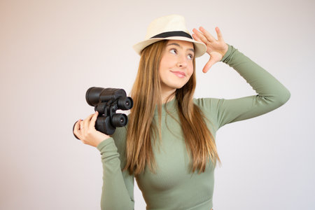 young girl with green sweater and straw hat smiling with binoculars on isolated white backgroundの写真素材