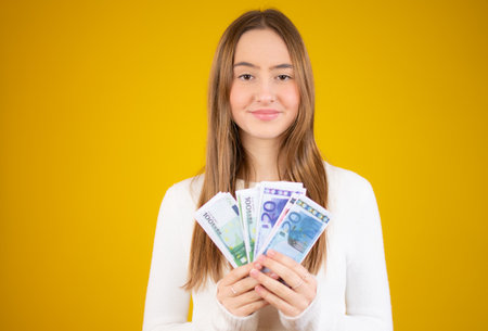 Young beautiful caucasian girl smiling holding money over yellow background