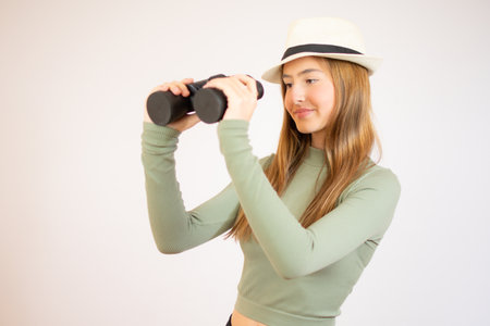 young girl with green sweater and straw hat smiling with binoculars on isolated white backgroundの写真素材
