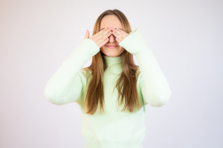 Young woman covering her eyes with her hands over white backgroundの写真素材