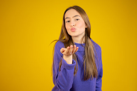 Portrait of cute lovely girl in casual outfit with modern hairdo sending blowing kiss with pout lips looking at camera isolated on yellow background. Affection feelings conceptの写真素材