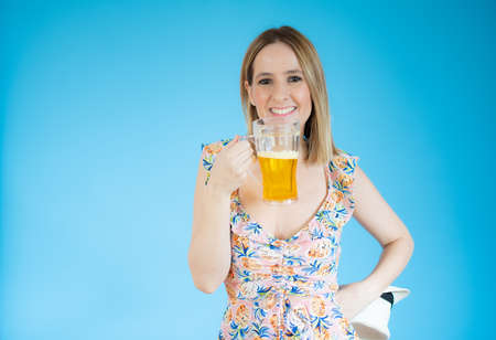 Beautiful young woman holding glass of beer over blue background.