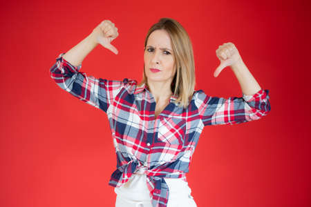 Young caucasian woman isolated on red background showing thumbs downの写真素材
