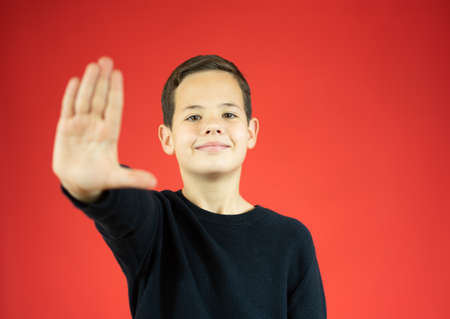 Happy caucasian boy making a gesture of stop with his palm over red backgroundの写真素材