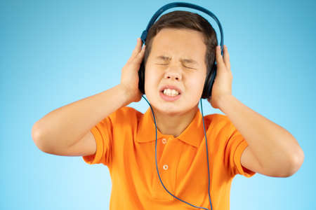 Attractive cute boy listening to music and holding hands on headphones on a blue backgroundの写真素材
