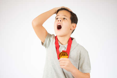 Young boy surprised showing his golden medal over white background.