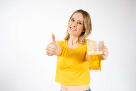 Cheerful young woman holding a beer mug full of beer and smiling over white backgroundの写真素材