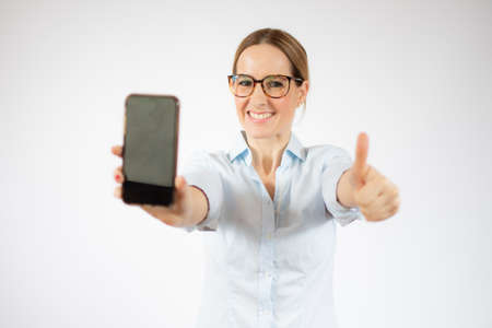 Young business woman showing smart phone with thumb up over white background.