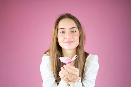 Young smiling girl holding a flower over pink background.