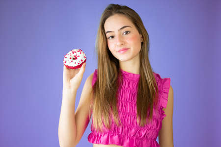 Beautiful girl holding donuts an having fun isolated over purple background. People with sweets.