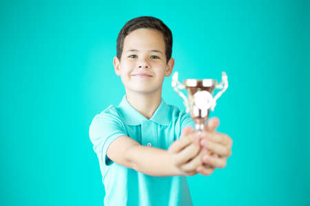 young boy holding a trophy with celebrating pose over green backgroundの写真素材