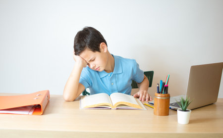 A young boy learning over his homework reading his workbook.の写真素材