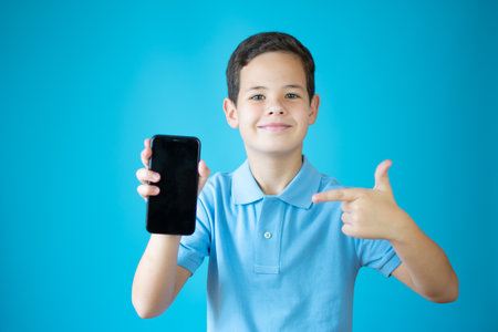Young caucasian boy showing okay gesture with phone isolated over blue backgroundの写真素材