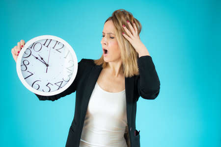 Business woman holding big clock in hands with worried gesture over green background.の写真素材