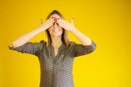 Pretty caucasian woman covering her eyes with both hands over yellow background.