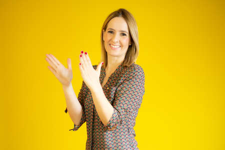 young pretty woman feeling happy and successful, smiling and clapping hands, saying congratulations with an applause over yellow background.の写真素材