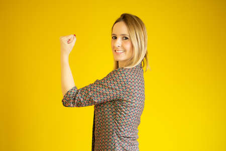 Successful woman raising hand in success gesture over yellow background
