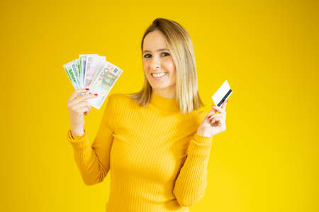 Portrait of an excited young woman holding money banknotes isolated over yellow background