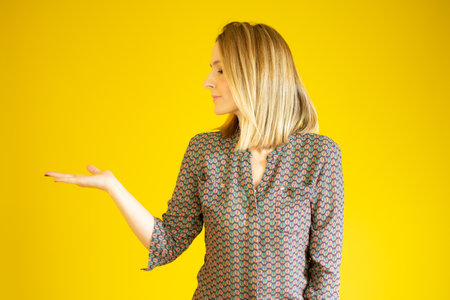 Smiling young woman showing something, some product or blank copy space area for advertise slogan or text message over yellow background.の写真素材