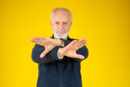 Grey bearded hair senior over yellow background Rejection expression crossing arms and palms doing negative signの写真素材