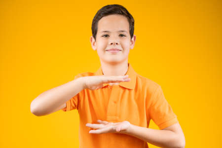 Beautiful young boy over isolated orange background smiling, showing and pointing something that is on her handの写真素材
