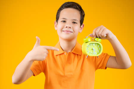 childhood, fashion and people concept - portrait of happy smiling boy in orange shirt with alarm clock over orange backgroundの写真素材