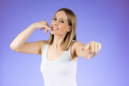 Young woman over isolated purple background making phone gesture. Call me back sign.