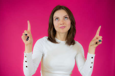Portrait of beautiful young woman pointing up over pink background.の写真素材