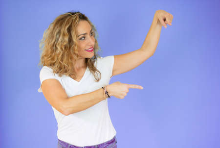 Young blonde woman with curly hair wearing casual white t-shirt pointing down with fingers showing...