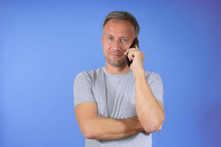 Young handsome man in casual t-shirt over isolated purple background keeping a conversation with the mobile phoneの写真素材