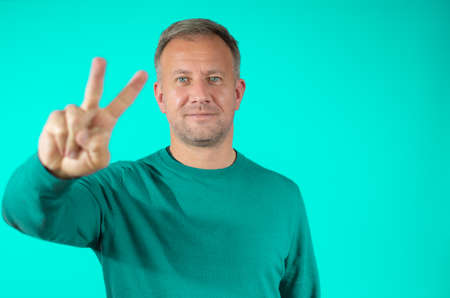 Portrait of an adult man smiling and showing you victory sign against green backgroundの写真素材