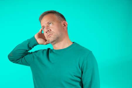 Young handsome man wearing casual sweater standing over green background confuse and wonder about question. Uncertain with doubt, thinking with hand on head. Pensive concept.の写真素材
