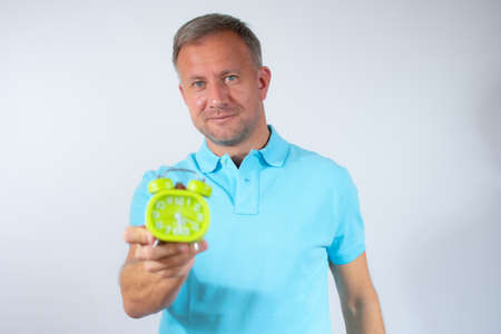 Young man holding an alarm clock over white background.の写真素材