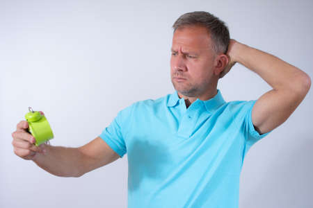 Young man holding an alarm clock over white background.の写真素材