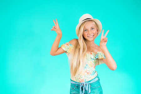 Portrait of a blonde girl in summer clothes making the victory gesture over green backgroundの写真素材