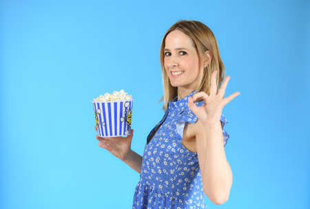 Image of happy cute young woman standing isolated over blue background eating popcornの写真素材