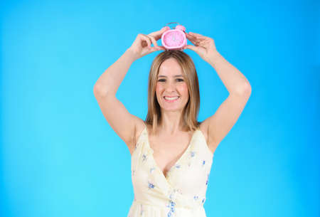 Young woman holding alarm clock on head standing over isolated blue background very happyの写真素材
