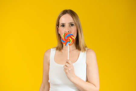 Young woman holding a big lollipop over isolated over yellow background.の写真素材