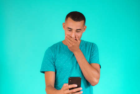 Surprised young latin man using mobile phone over green background.の写真素材