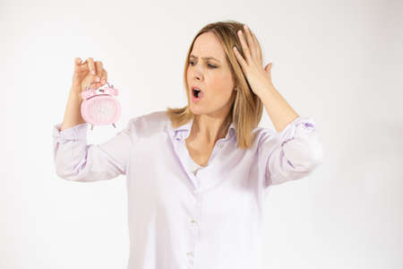Portrait of amazed young woman holding alarm clock isolated over white background